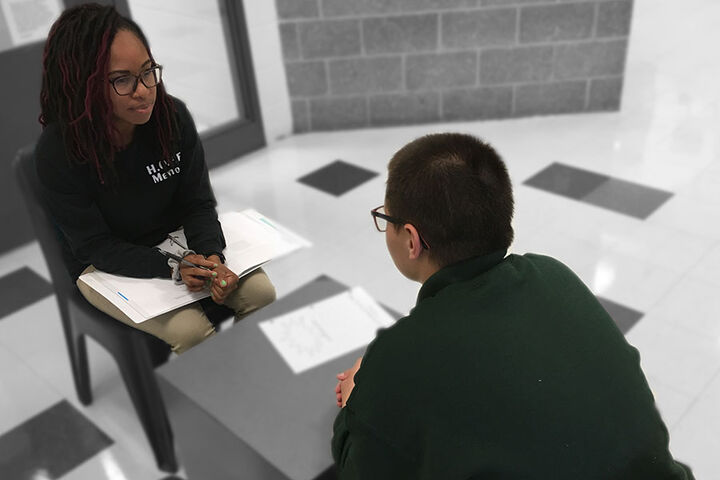A college student mentor and her mentee sit and converse at a table.